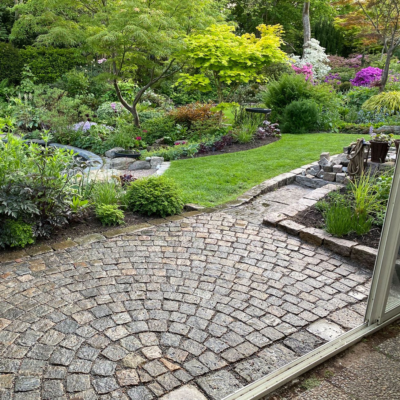 Välskött trädgård med stenläggning och färgglada växter.
